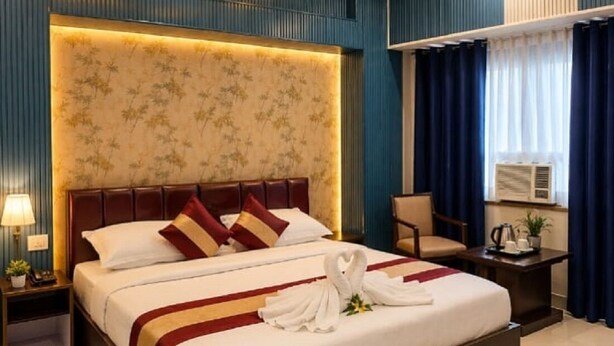 Een hotelkamer met een groot bed, een plafondventilator, een nachtkastje, een bureau en een raam met gordijnen.
