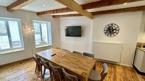 Ein Essbereich mit Holztisch und Stühlen, einem an der Wand befestigten Fernseher und einer Heizung.