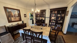 Un coin repas avec une table dressée pour quatre personnes, entourée de chaises, d’un lustre et d’une bibliothèque remplie de livres.