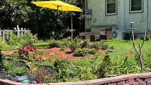 Un jardin avec un mur en briques, un parasol jaune et un bâtiment en arrière-plan.