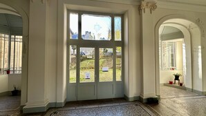 A grand entrance with a large glass door, a tiled floor, and a view of a garden with a sign. - Le Métropole 410 La Bourboule (La Bourboule)