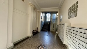 A hallway with a patterned floor, a staircase, and a row of mailboxes on the right. - Le Métropole 410 La Bourboule (La Bourboule)