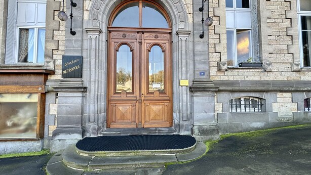 A historic building with a large wooden double door, a stone facade, and a small step with a black mat. - Le Métropole 410 La Bourboule (La Bourboule)