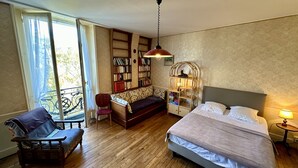 A bedroom with a bed, a chair, a sofa, a bookshelf, and a balcony with a railing. - Le Métropole 410 La Bourboule (La Bourboule)