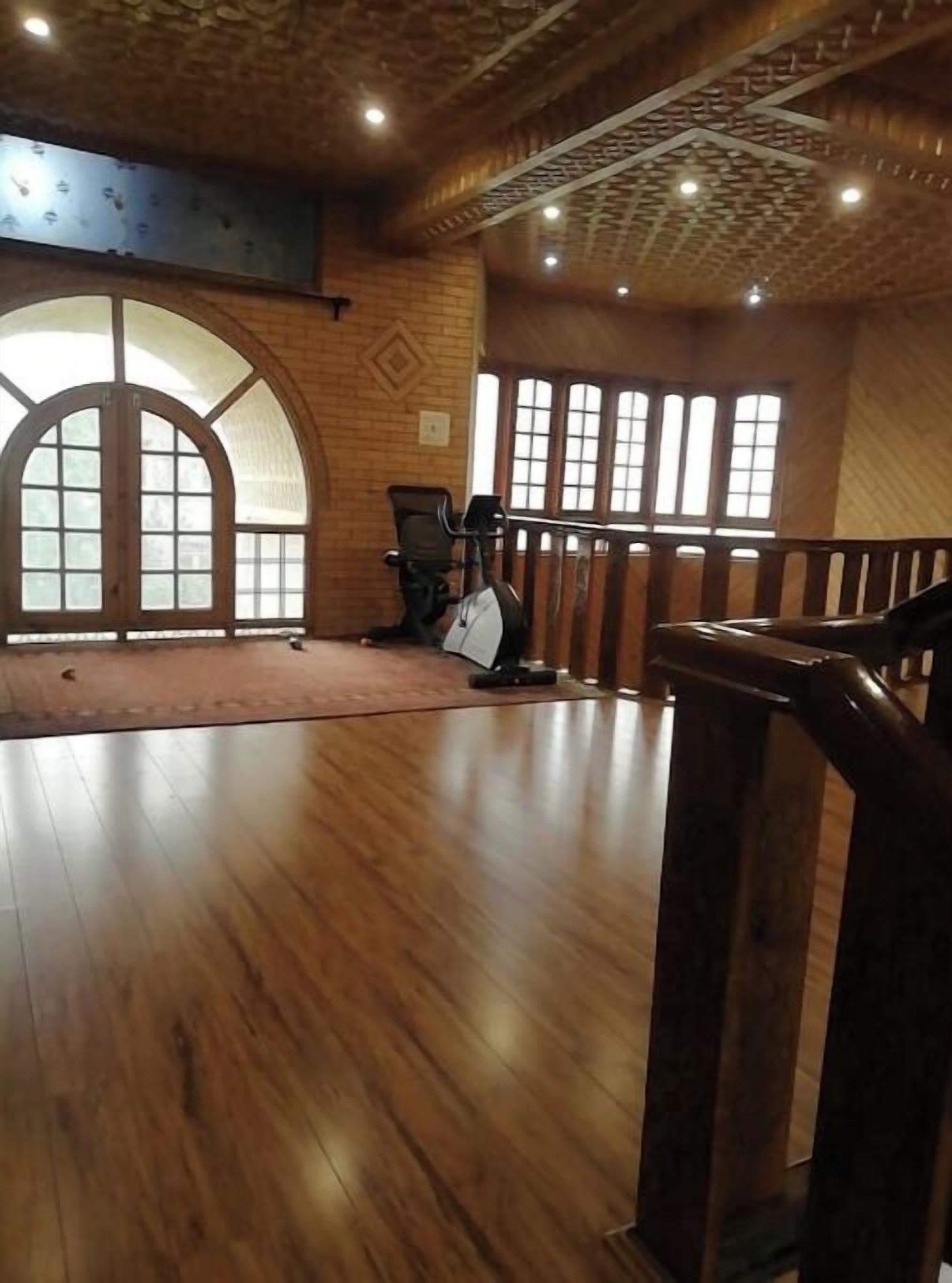 A spacious room with wooden flooring, a large arched window, and a staircase with a wooden railing.