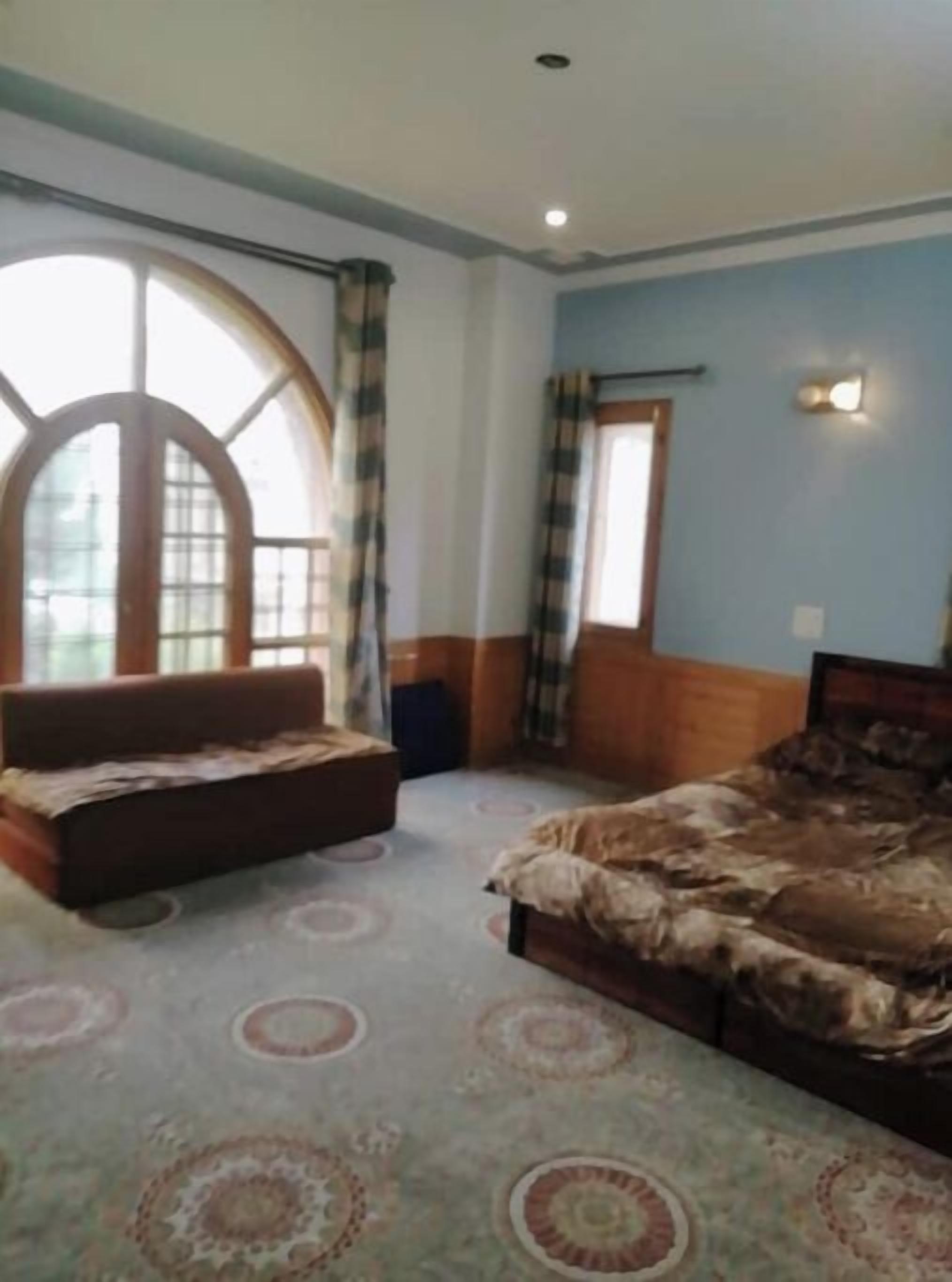 A bedroom with a large arched window, a bed with a patterned bedspread, a sofa, and a carpet with circular patterns.