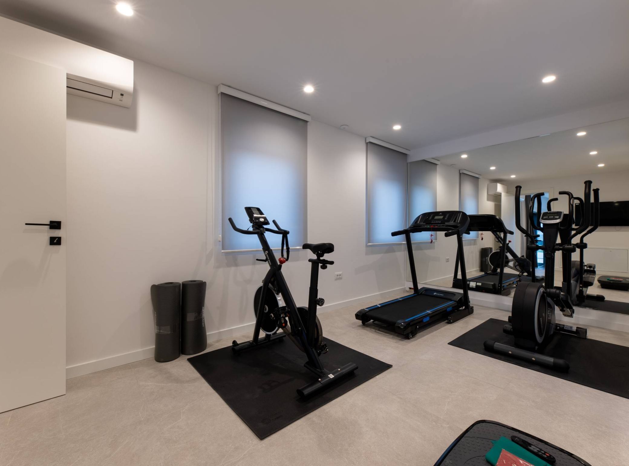 Ein Heim-Fitnessraum mit Fahrradergometer, Laufband, Crosstrainer und Gewichten.