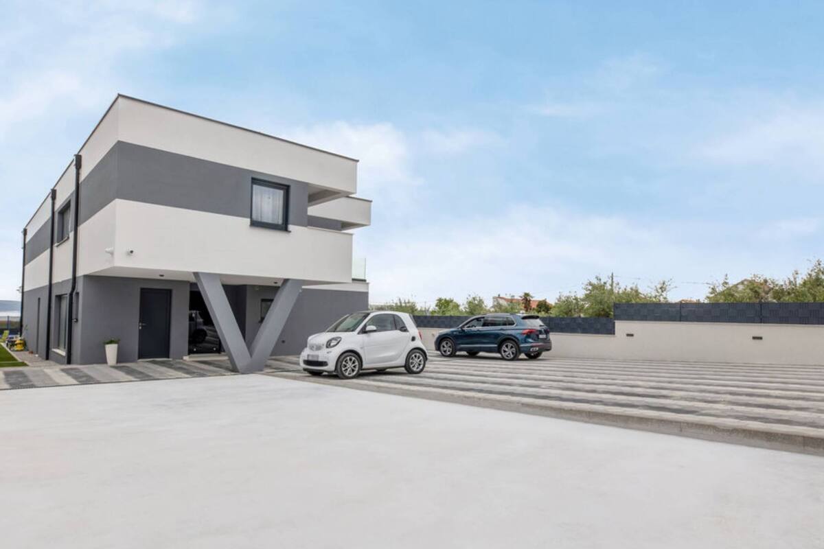Ein modernes, zweistöckiges Gebäude mit Garage, zwei geparkte Autos davor und blauem Himmel.
