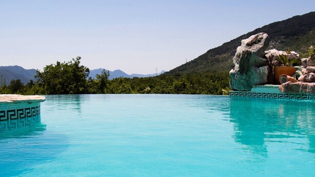 A clear blue pool with a decorative edge, surrounded by greenery and mountains in the background. - Authentic Dalmatian Hillside Escape With Pool, Sauna & BBQ (Sestanovac)