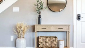 Een trap met witte leuningen, een console tafel met spiegel, een vaas met gedroogde planten, een rieten mand, en een klein witte bakje met een pootafdruk.