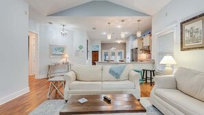 A spacious living room with a high ceiling, a kitchen in the background, and a dining area.