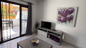 A modern living room with a ceiling fan, a flat-screen TV, a coffee table, and a sliding glass door leading to an outdoor area.