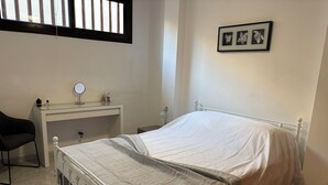 A bedroom with a bed, a desk, a chair, and a window.