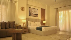 A modern hotel room with a large bed, a sofa, a wooden side table, and a small table. - Settle Inn Janoub Apartments (New Cairo)