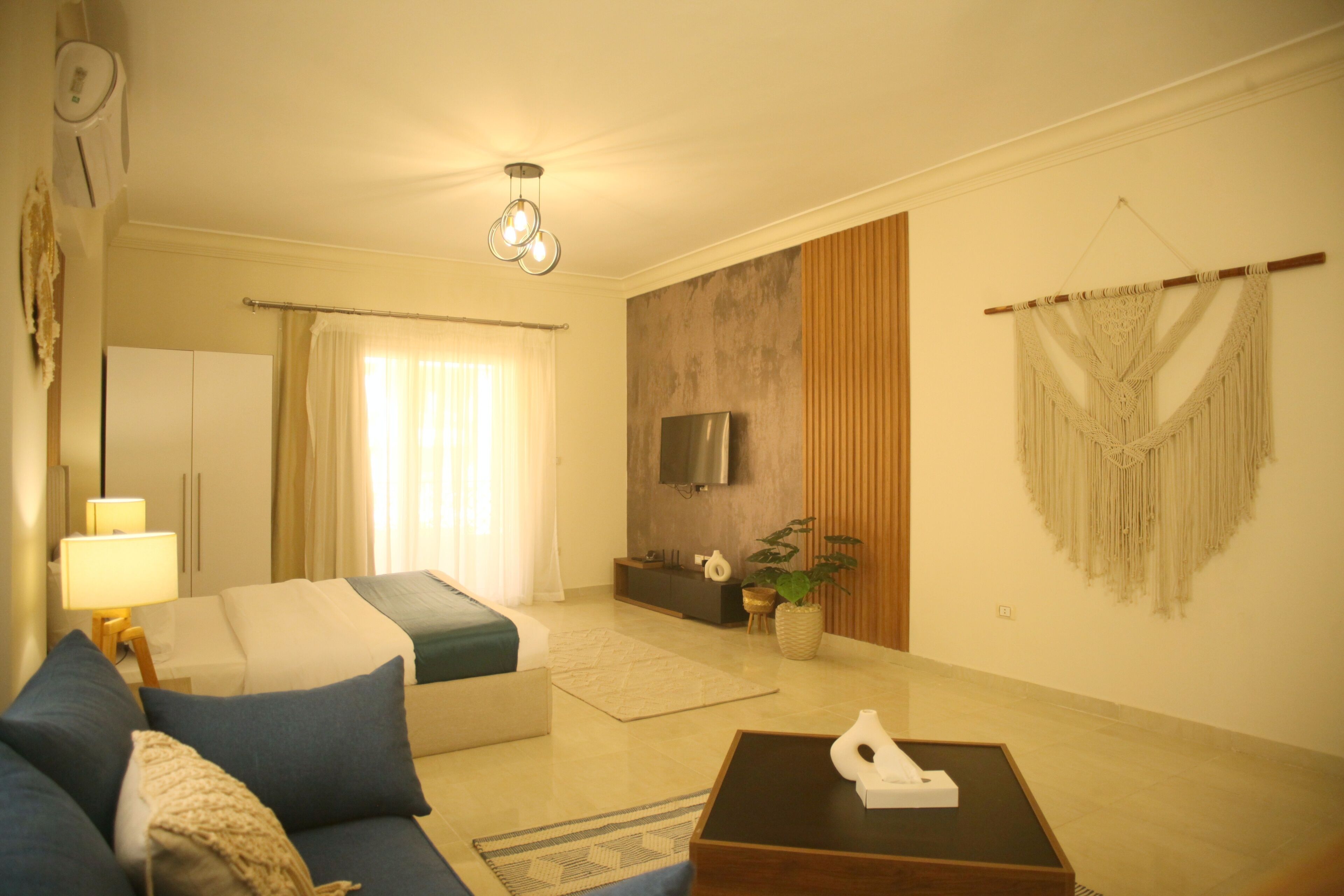 A modern living room with a sofa, a coffee table, a TV, and a decorative macrame wall hanging.