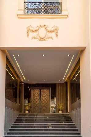 A grand entrance with a staircase, ornate wall decorations, and a large door. - Settle Inn Janoub Apartments (New Cairo)