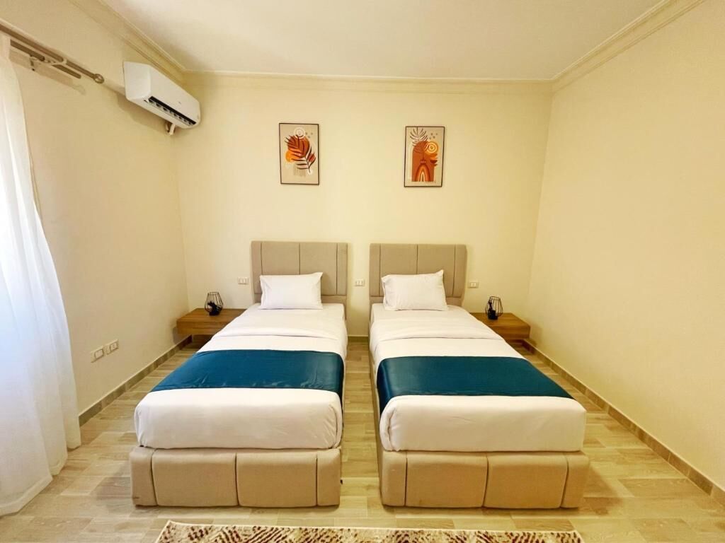 A room with two beds, a ceiling fan, and two wall-mounted air conditioning units.