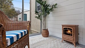 A wicker chair with a striped cushion, a potted plant, and a wood-burning stove in a corner. - "The Darling" at Drew by Roxy Rentals (Minneapolis)
