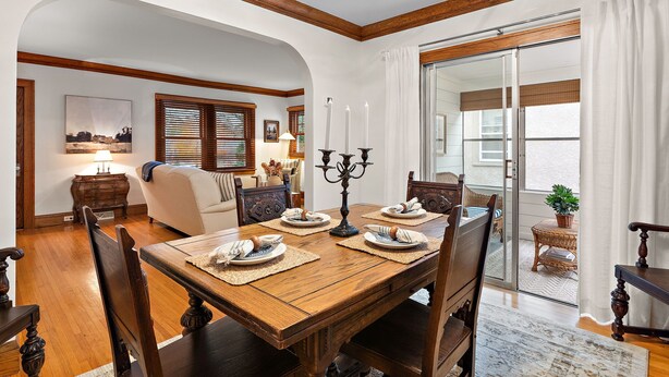 A dining room with a wooden table set for four, a chandelier, and a view of the outdoors through a sliding glass door. - "The Darling" at Drew by Roxy Rentals (Minneapolis)