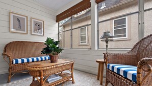 A wicker sofa with a blue and white cushion, a wicker table with a plant, and framed artwork on the wall. - "The Darling" at Drew by Roxy Rentals (Minneapolis)