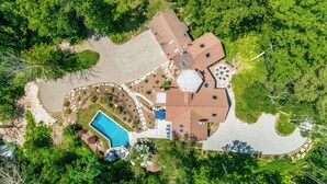 An aerial view of a residential property with a swimming pool, patio, and surrounding greenery.