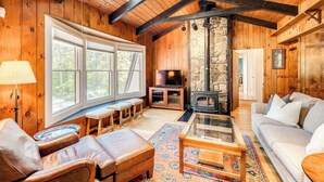 A cozy cabin interior with wooden walls, a stone fireplace, a sofa, a coffee table, and a television.