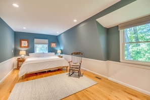 A bedroom with a bed, a chair, a window, and a nightstand with a lamp.