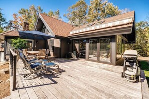 A wooden deck with outdoor furniture, a barbecue grill, and a glass-enclosed patio area.