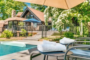 A poolside area with a metal chair, a table with towels, and a house in the background.
