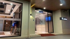 Entrada de hotel con puerta de vidrio, interior visible y una persona sentada, con un letrero que indica el nombre del hotel.
