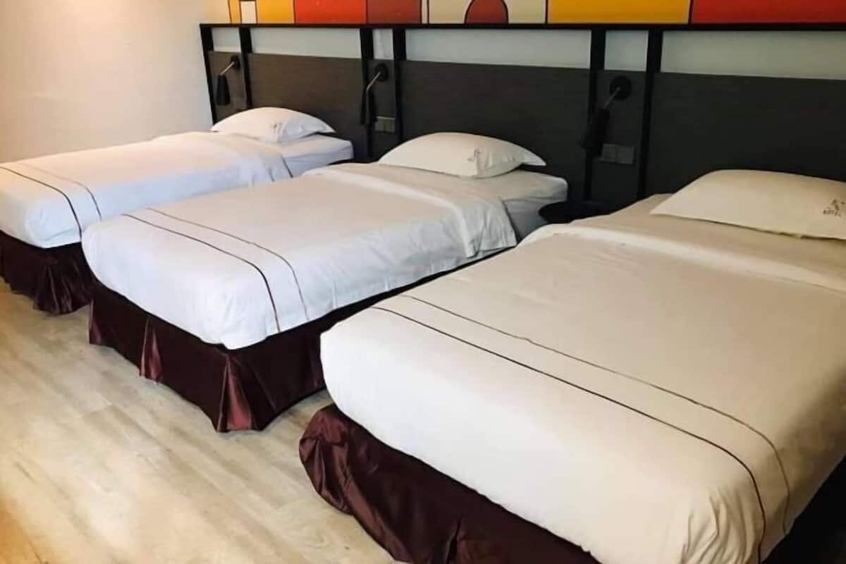 A hotel room with three single beds, each with a brown skirt and white bedding.