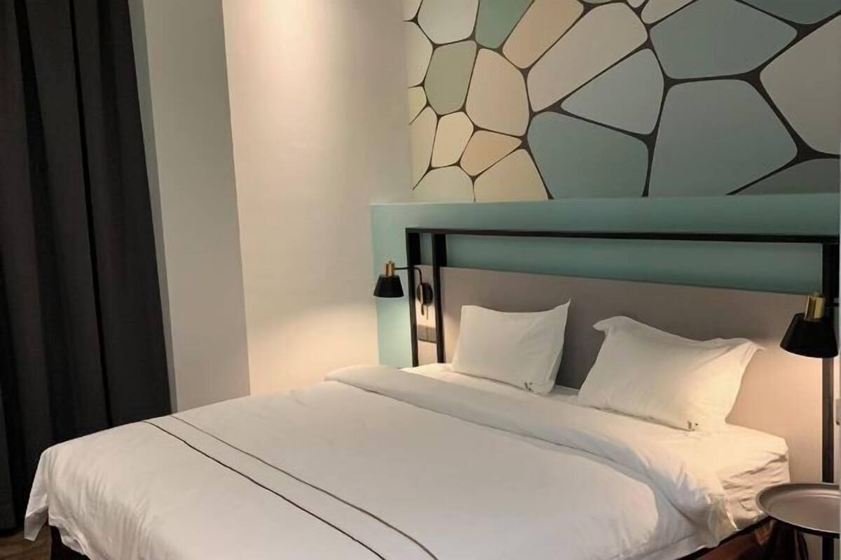 A neatly made bed with white linens, a modern headboard, and a wall art piece above it.
