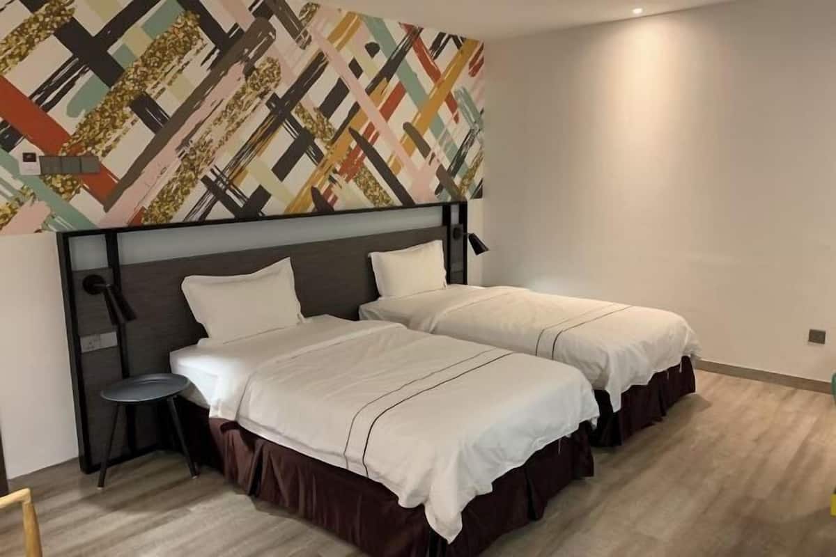 A hotel room with a bed, a small stool, and a wall with a geometric pattern.