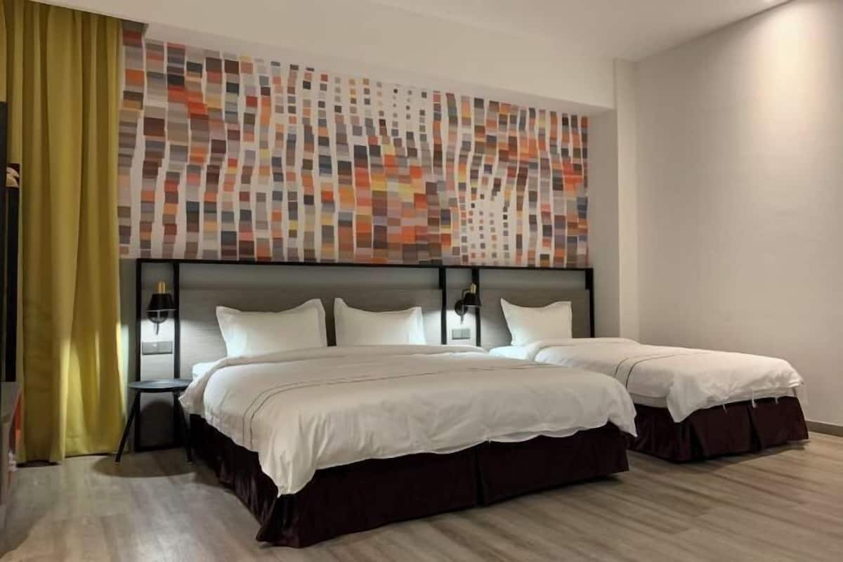 A hotel room with two beds, a modern abstract wall art, a small table, and a lamp.