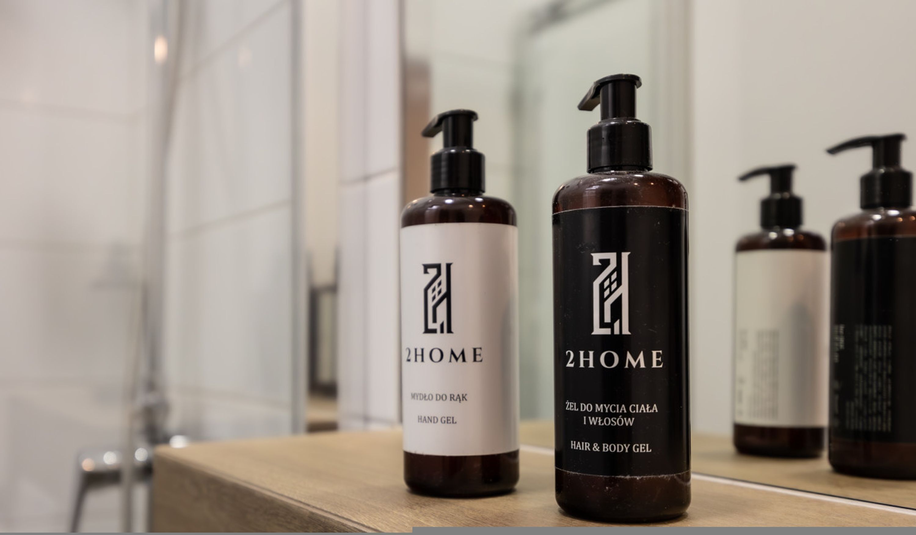 Two bottles of 2HOME hand and hair & body gel on a wooden surface.