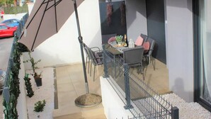 A modern outdoor patio with a dining table and chairs, a large umbrella, and a railing. - Stylish Okrug Gornji Apartment With Terrace and Patio (Okrug)