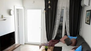 A living room with a sofa, a coffee table, a TV, and a sliding glass door leading to a balcony. - Stylish Okrug Gornji Apartment With Terrace and Patio (Okrug)
