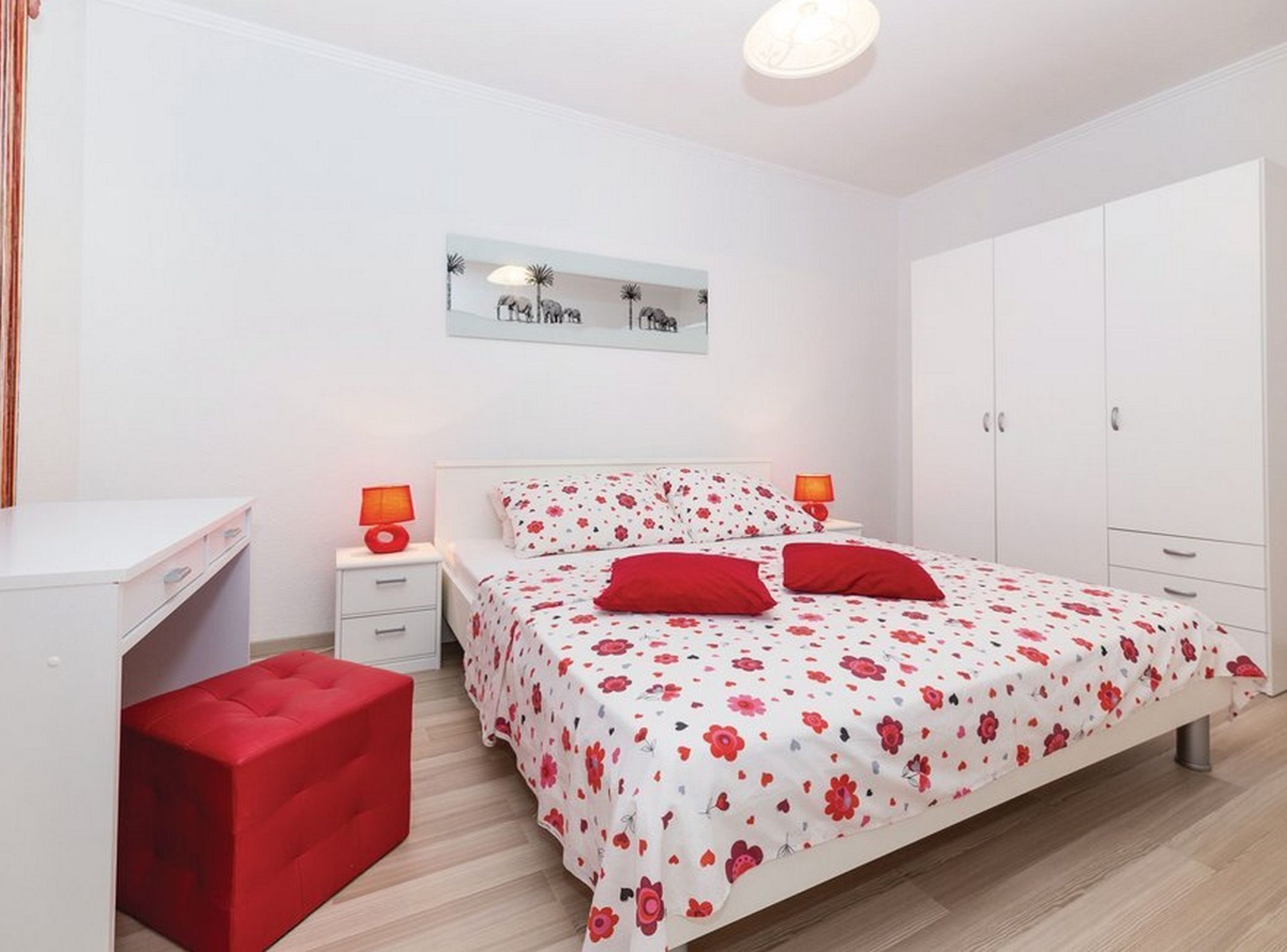 A bedroom with a bed, two bedside tables, a desk, a red bench, and a wardrobe.