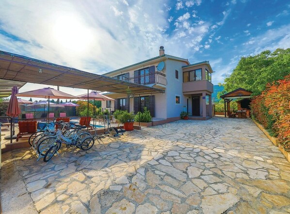 Una casa de dos pisos con un patio de piedra, mobiliario exterior y una piscina.