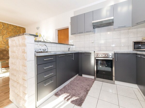 A modern kitchen with grey cabinets, a built-in oven, and a stone accent wall.