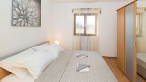 Un dormitorio con cama, mesita de noche con lámpara, ventana con cortinas y armario.