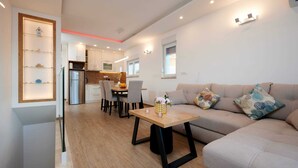 Ein modernes Wohnzimmer mit einer Couch, einem Esstisch mit Stühlen und einer Küche im Hintergrund.