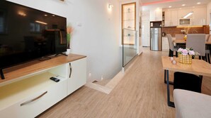 Eine moderne Küche mit integriertem Backofen, Mikrowelle und Kühlschrank. Es gibt einen Essbereich mit Tisch und Stühlen sowie einen Fernseher auf einem Holzboden.