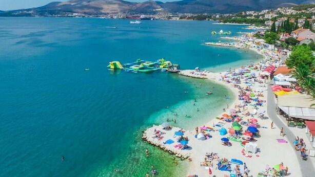 Una playa costera con aguas azules cristalinas, una orilla arenosa y algunas embarcaciones.