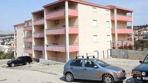 Un edificio residencial de varios pisos con balcones, un estacionamiento y un sello de fecha.
