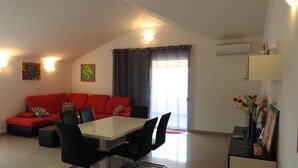 Una sala de estar moderna con un sofá rojo, una mesa de comedor con sillas y un gran ventanal con cortinas.