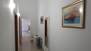 Un pasillo con una puerta que da a una habitación, una pequeña mesa con un florero y un cuadro enmarcado en la pared.