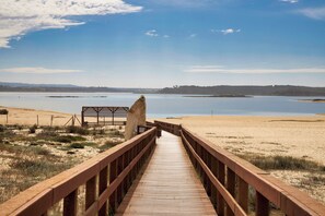 A wooden boardwalk leading to a sandy beach area with a clear view of a calm body of water and distant hills. - Discover a paradise: stunning beaches, golf courses and historic sites (Costa de Santo André)