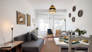 Una sala de estar moderna con un sofá gris, una mesa de comedor con sillas y una zona de cocina al fondo.