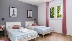 A bedroom with two single beds, a window with pink curtains, and two framed pictures on the wall.